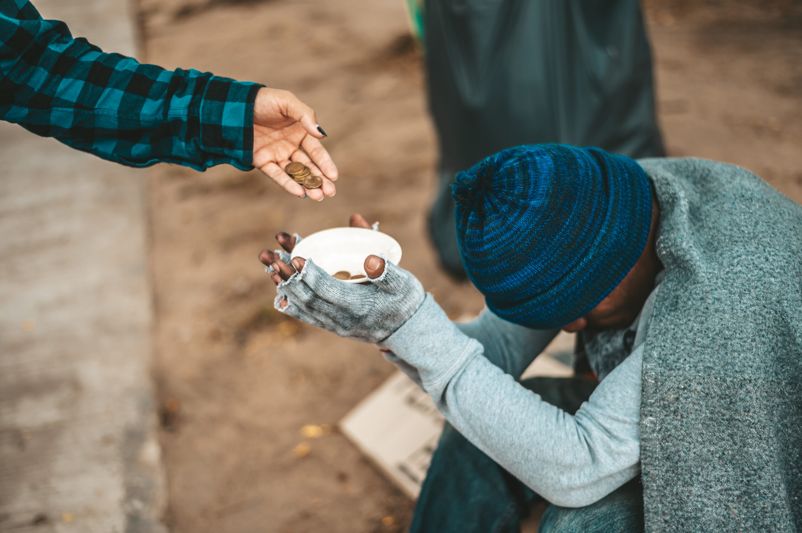 A young woman is handing money as zakat to a humbled beggar in the street.
